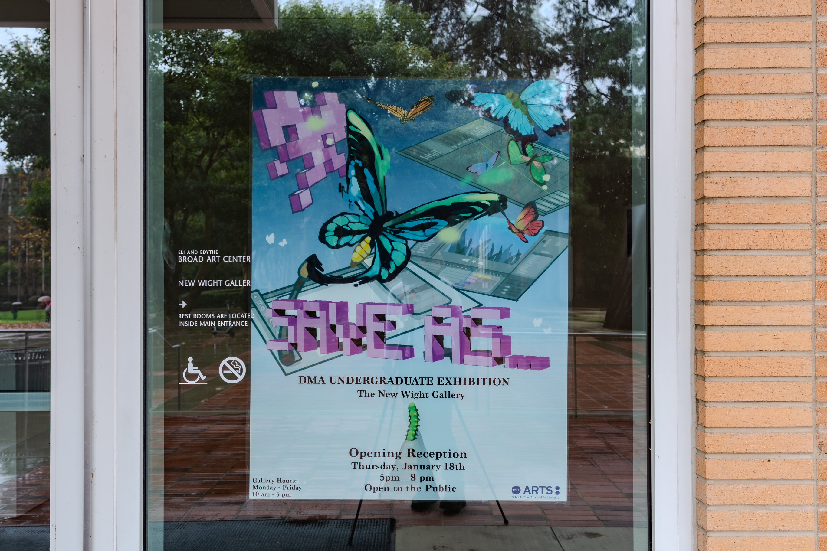 A promotional poster hanging on a glass window, the poster advertises the SAVE AS... DMA UNDERGRADUATE EXHIBITION in the New Wight Gallery.